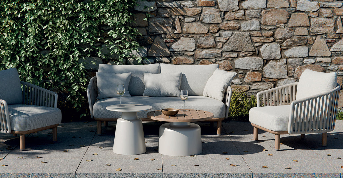 Outdoor patio set from Royal Garden with gray sofa, chairs, and tables against a stone wall.